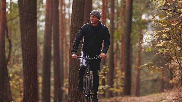 Man in trainingskleren op een fiets in het bos.
